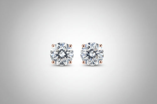 Diamond stud earrings held between fingers against a neutral background